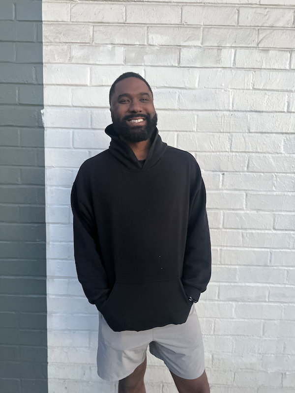 Photo of Mike Hardin smiling while standing in front of a white brick wall.